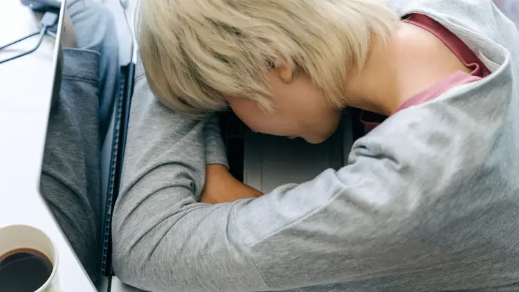 Woman resting her head on her arms at a desk beside a laptop