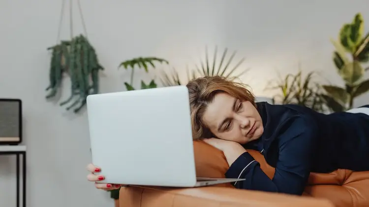 Tired woman resting her head on her arm beside an open laptop