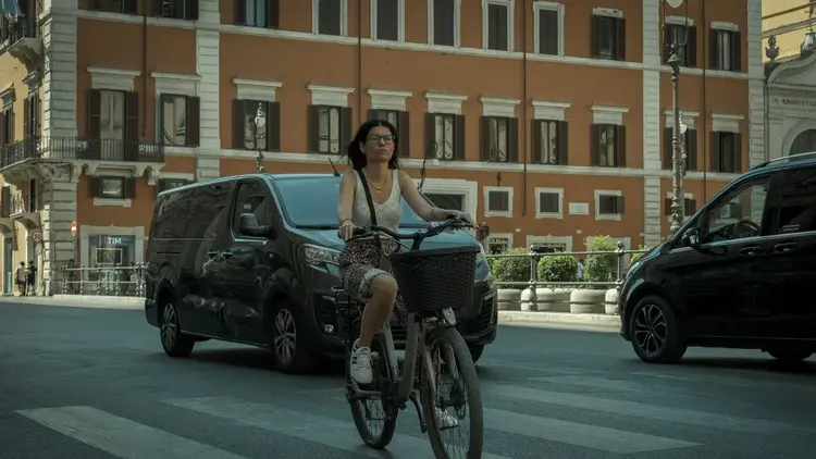 Woman cycling across a wide city street past parked vans