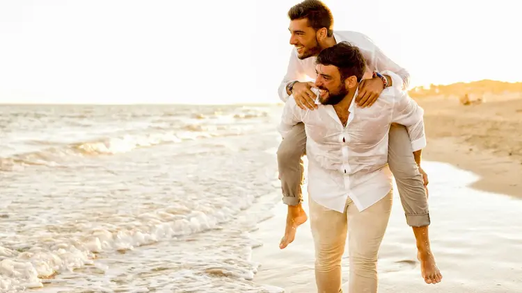 Man giving his partner a piggyback along the water's edge at sunset