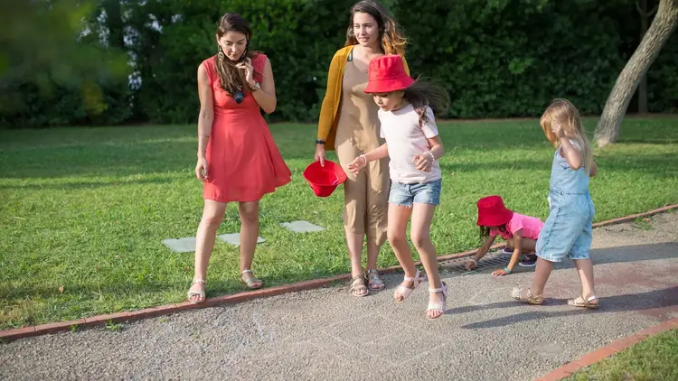 Two women walking through a park with three young children