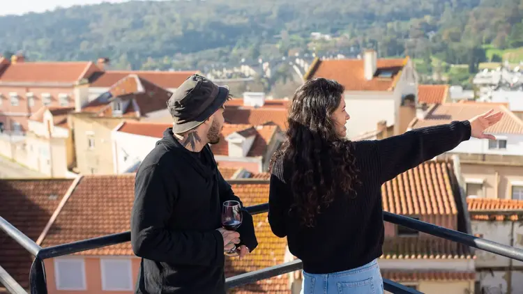 Two people on a terrace, one pointing out across red-tiled rooftops