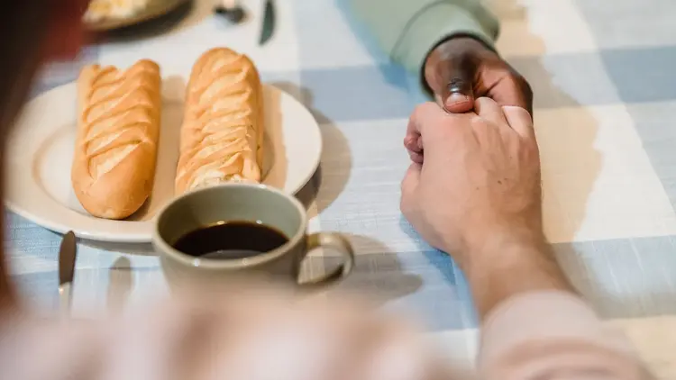 Two people holding hands across a breakfast table set with bread and coffee