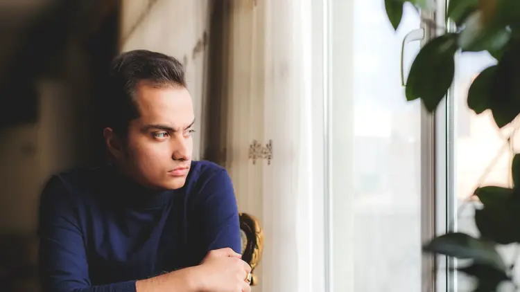 Young man in a navy jumper looking out of a window