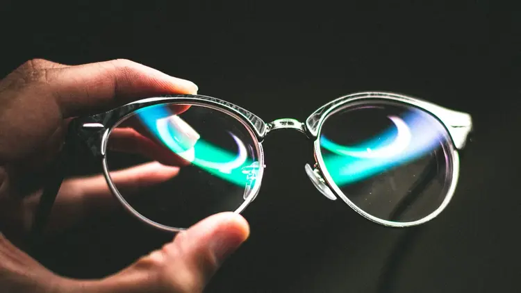 Hand holding a pair of glasses up to the light against a dark background