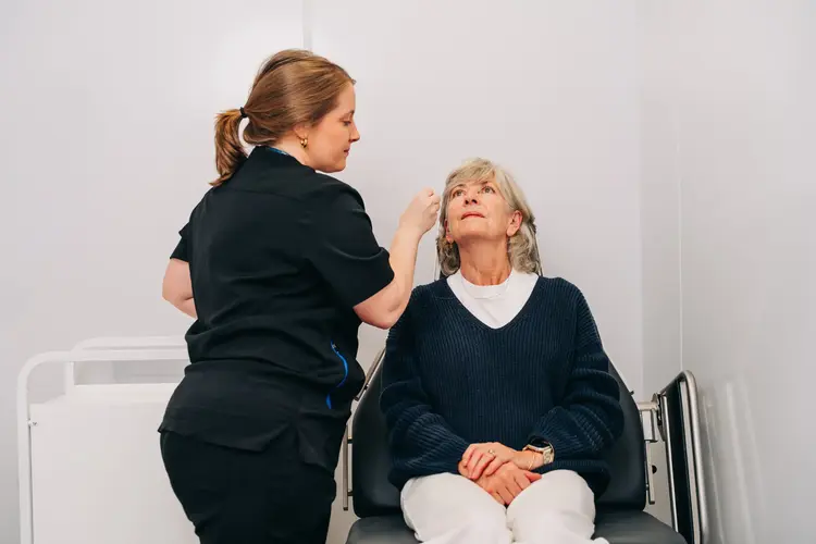 A healthcare professional in black scrubs preparing an elderly patient for an eye surgery.