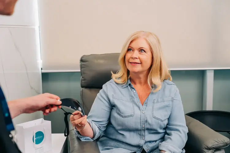 Smiling woman receiving glasses from a clinician after lens replacement