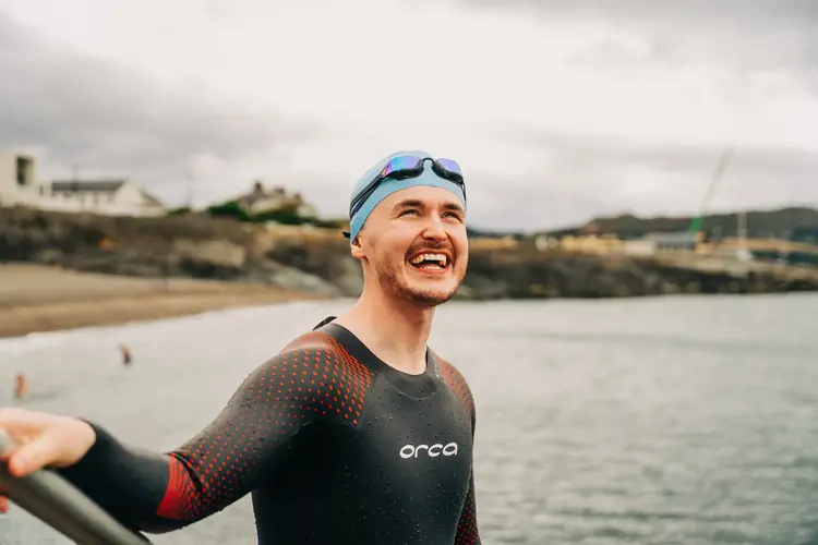 Smiling swimmer in a wetsuit and swim cap on a beach
