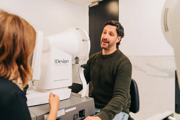 Man talking with an eye care professional beside an iDesign diagnostic machine