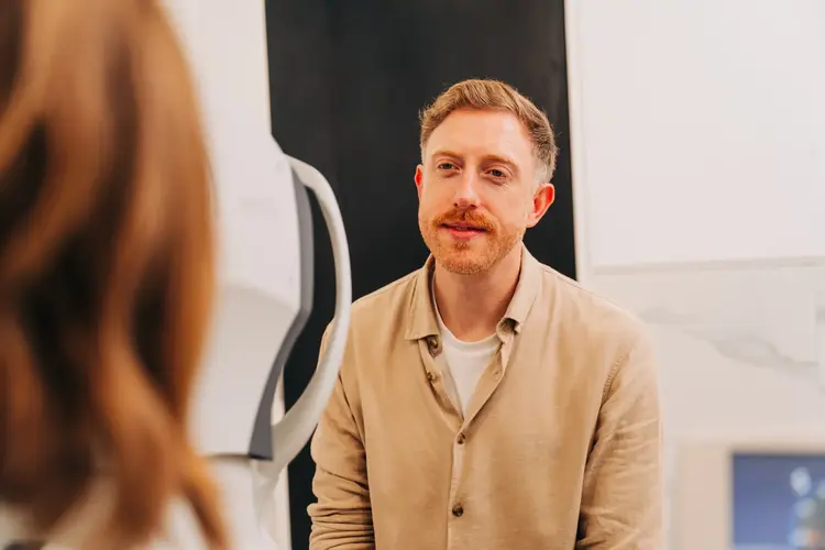 Man in beige shirt speaking with a woman during an eye exam consultation at Optilase Eye Clinic.