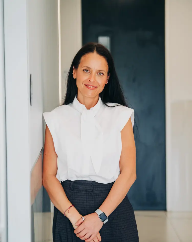Smiling woman with dark hair standing against a light wall