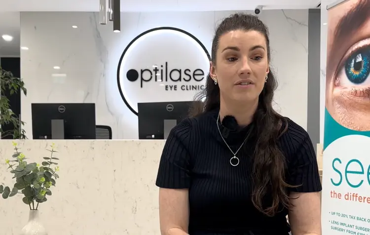 Woman in black top speaking at Optilase Eye Clinic reception.