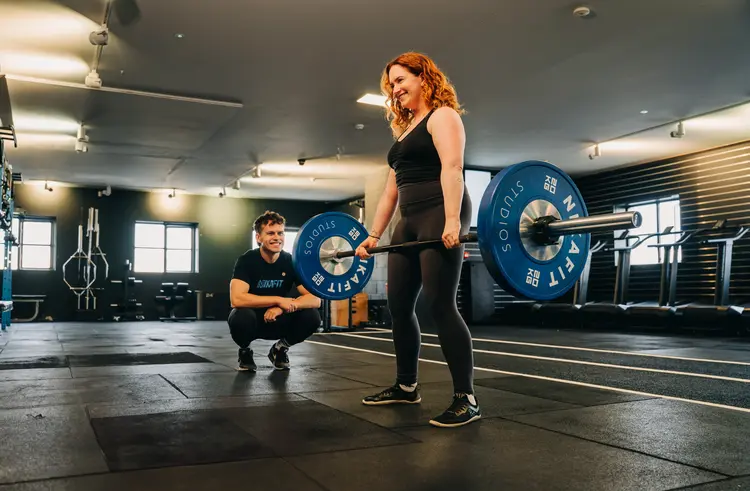 Woman lifting a barbell with her trainer after lens replacement surgery