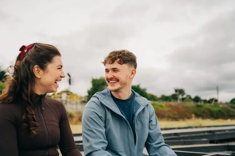 Two young adults smiling and laughing together outdoors on a cloudy day, after successful PRK.