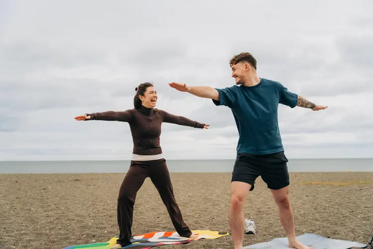 Two people laughing as they do yoga on a beach after laser eye surgery