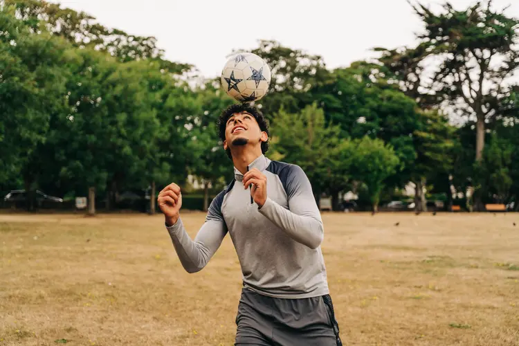 Young man balancing a football on his head in a park after LASIK