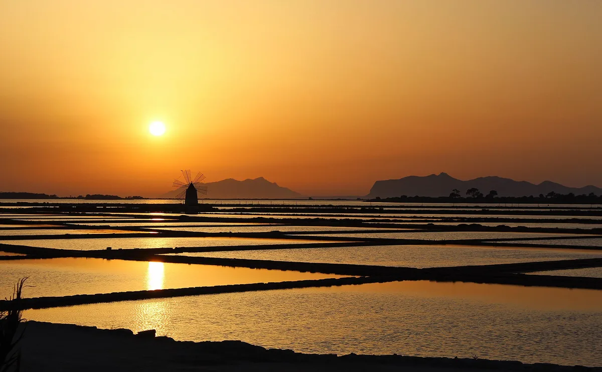 Bassins des salines de Marsala au coucher du soleil, reflets orange et diguettes de terre
