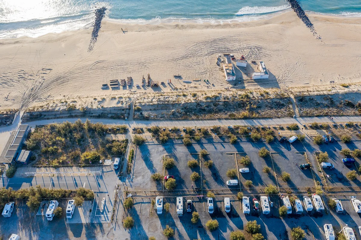 Vans et camping-cars alignés sur une aire de stationnement en bord de mer