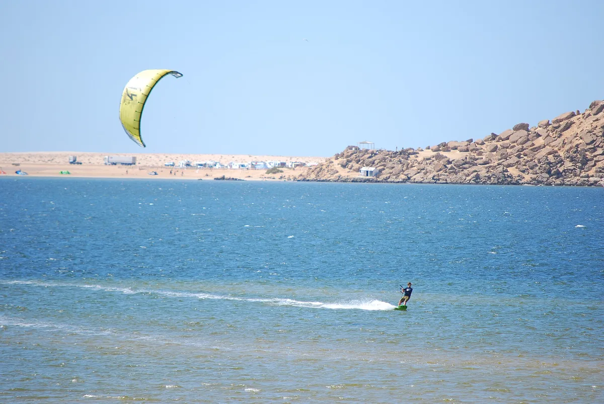 Un rider seul sur la lagune, la pointe rocheuse et les bâtiments d’un camp au fond