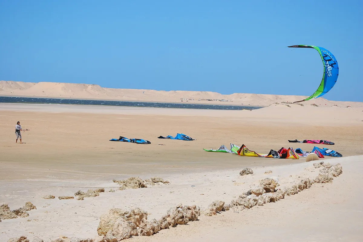Ailes de kite posées sur le sable au bord de la lagune, dune derrière