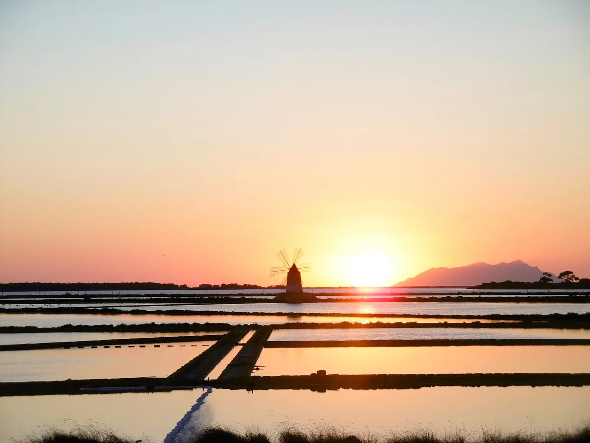 Les salines de la lagune au coucher du soleil, un moulin en silhouette et le mont Erice à l’horizon