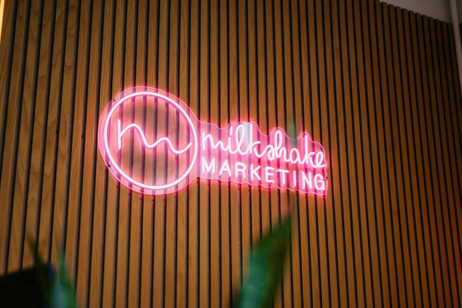 Het neonlogo van Milkshake marketing, een cirkel op de houten wand van ons kantoor