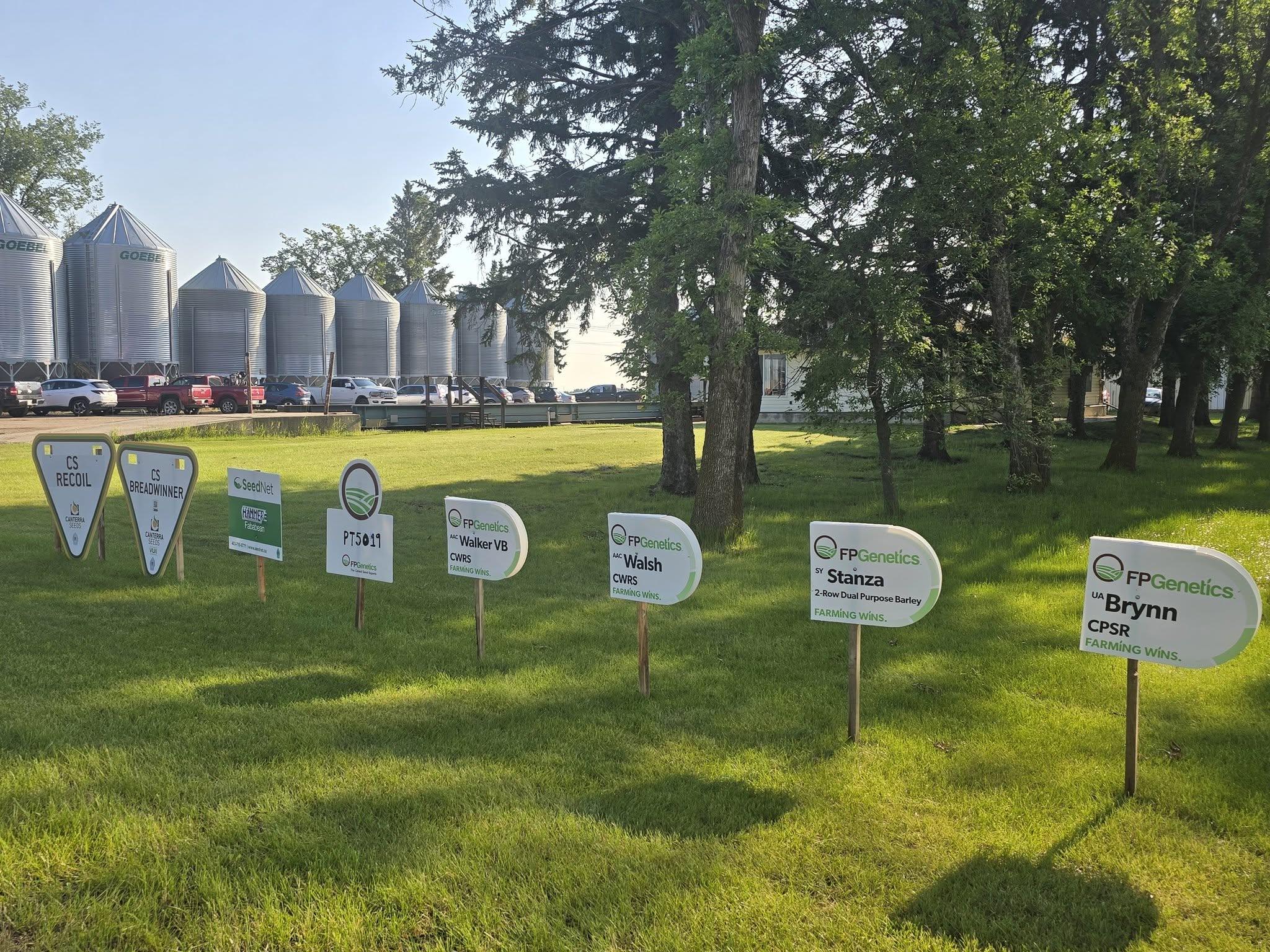 Variety trial plot signs staked in the grass beside the bins