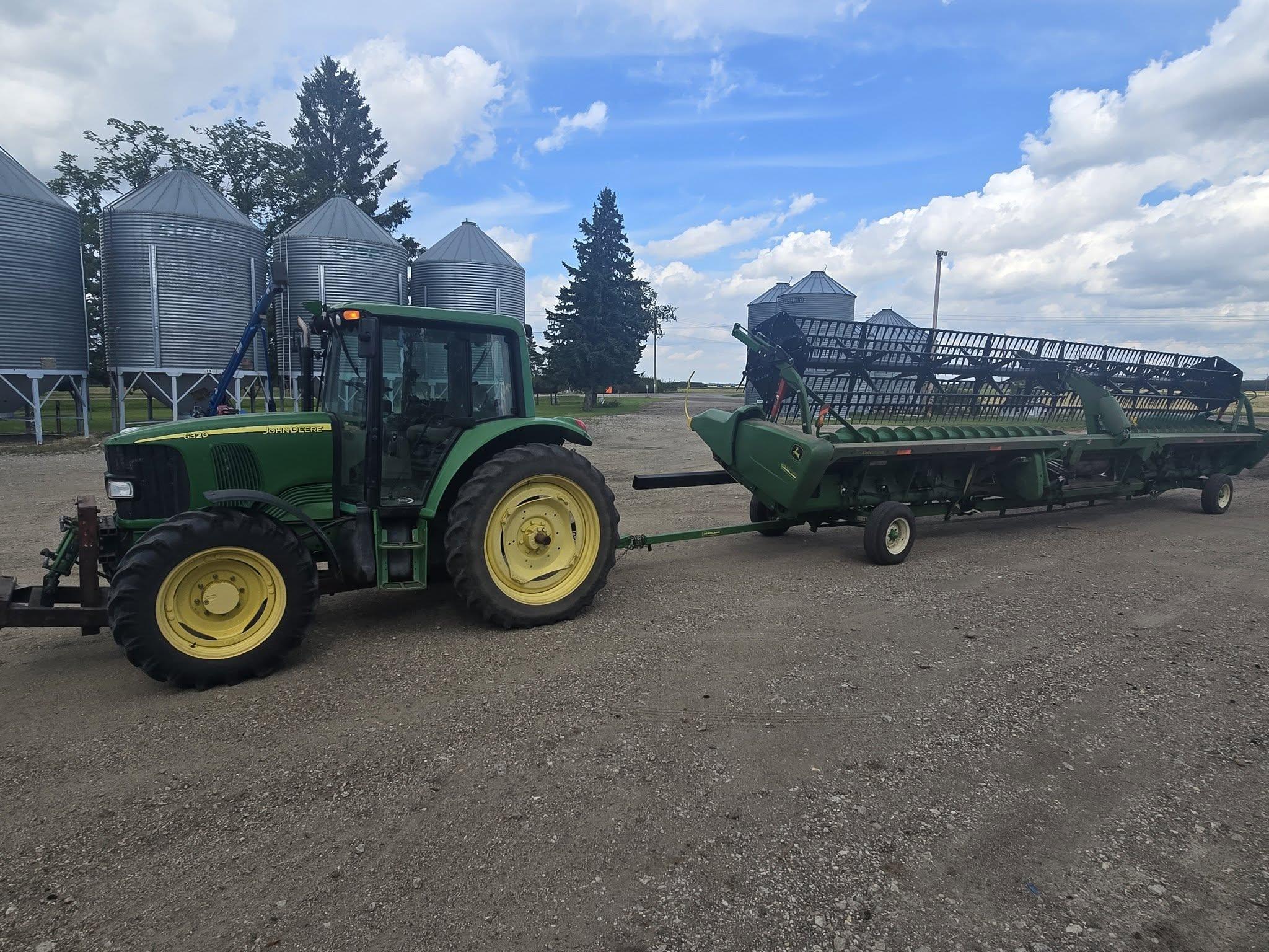 A tractor towing the draper header past the bin row