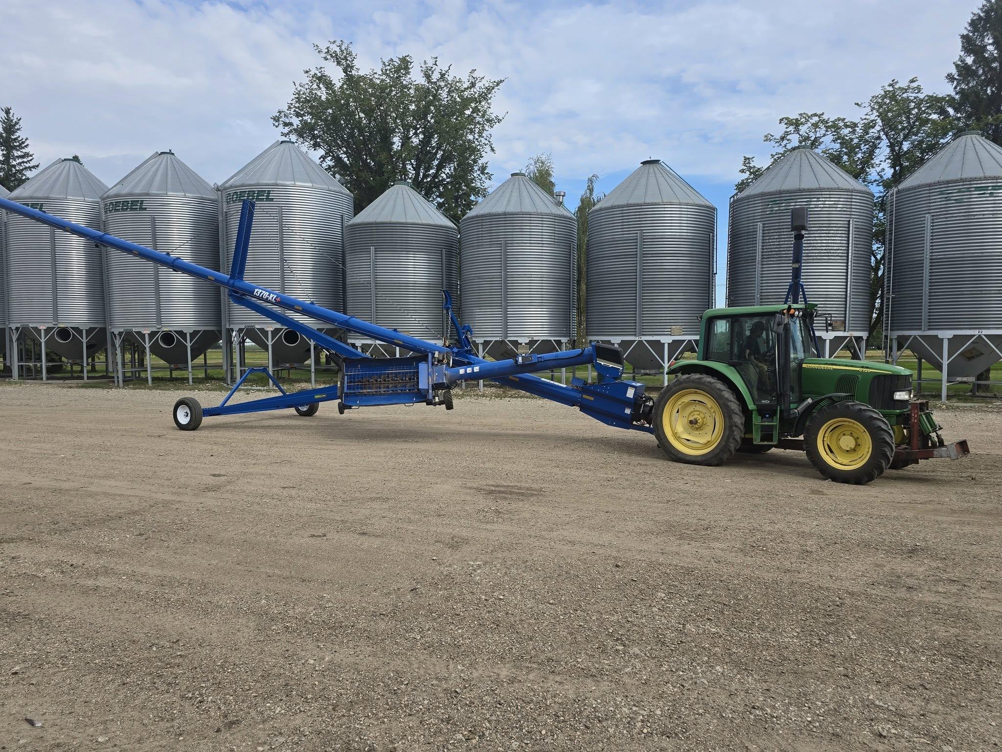 A grain auger and tractor lined up along the bins
