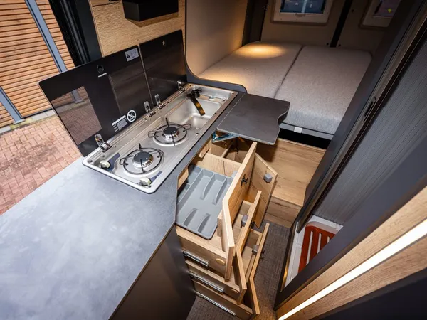 Roadstar X – Reisemobil-Küche mit Gaskochfeld, Spüle und ausziehbaren Schubladen, im Hintergrund Bett