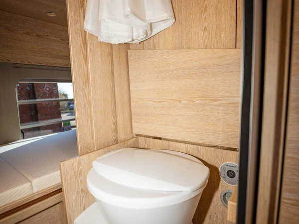 Vario 545 – Toilette im Badezimmer eines Reisemobils mit Holzvertäfelung und Bettansicht.