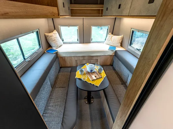 Avanti R – Gemütlicher Innenraum mit Sitzgruppe, Tisch und hinterem Bettbereich im Reisemobil.