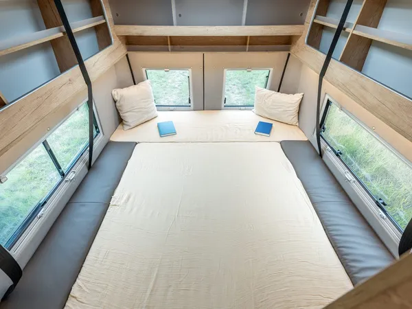 Avanti R – Bett im Reisemobil Avanti R, mit Kissen, Büchern und Fenstern.