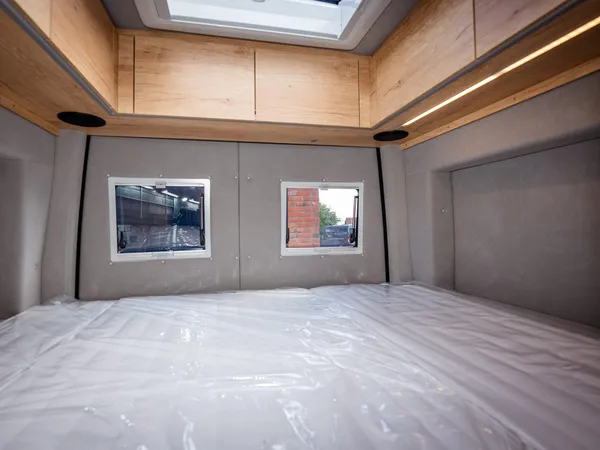 Regent S – Bett im Reisemobil mit zwei Fenstern und Oberschränken, noch in Folie.