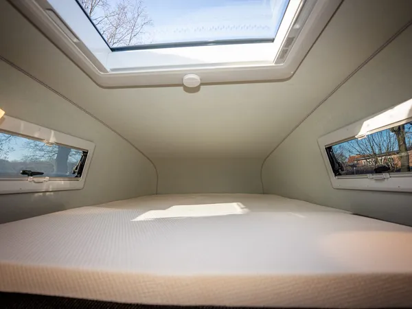 Vario 545 – Blick auf das bequeme Bett mit Fenstern und Dachluke im Reisemobil.