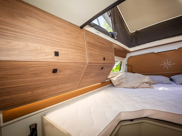 Columbus Liner – Bett im Reisemobil mit Holzeinbauten und geöffnetem Aufstelldach.