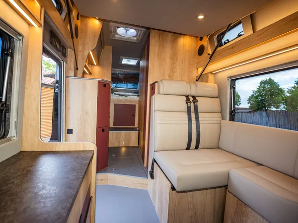 Nova M – Helle Sitzgruppe im Nova M Wohnmobil mit L-förmigem Sofa und Tischansatz.