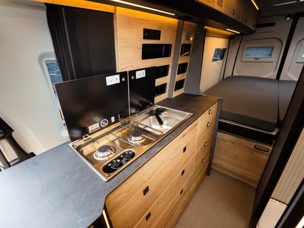 Roadstar XL Evo – Moderne Wohnmobilküche mit Kochfeld, Spüle und seitlichem Bettbereich.