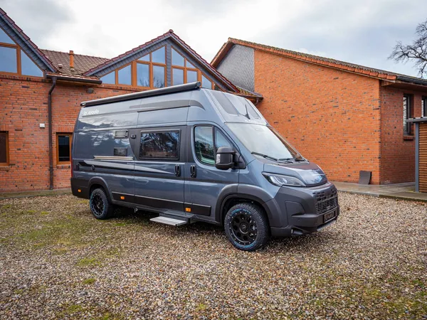 Avanti F – Graues Reisemobil Avanti F schräg von vorne auf Kies vor Haus.