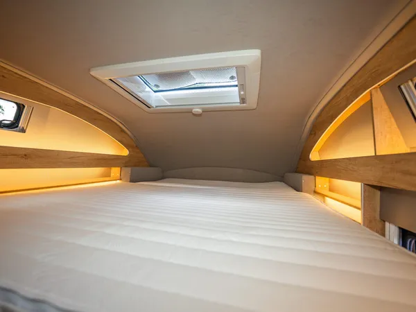 Nova M – Bettbereich im Reisemobil mit Matratze, Dachfenster und indirekter Beleuchtung.