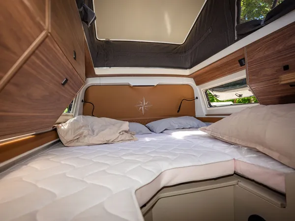 Columbus Liner – Bettbereich mit Matratze, Kissen und Holzelementen im Reisemobil.