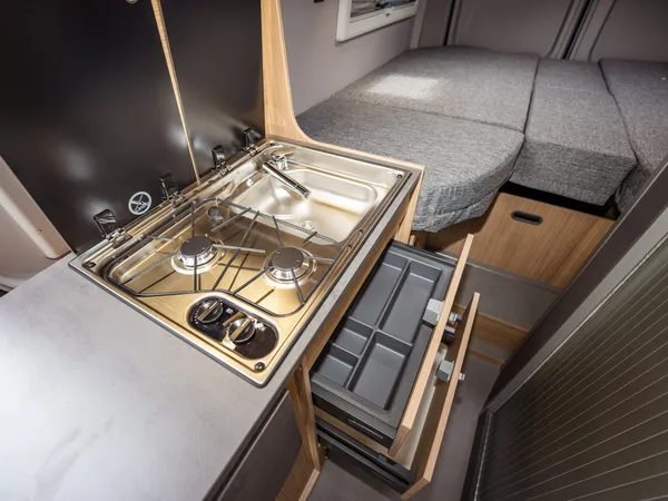 Summit Shine 600 L Elegance – Küche mit Kochfeld, Spüle und Auszug, daneben ein Bett im Camper.