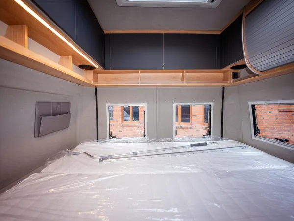 Avanti F – Blick auf das neue, in Folie verpackte Bett im Reisemobil Heckbereich.