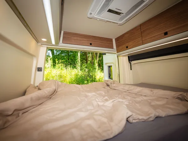 Sven Hedin 50 Jahre Edition – Bett im Reisemobil mit Blick auf grüne Natur durch offene Hecktür.
