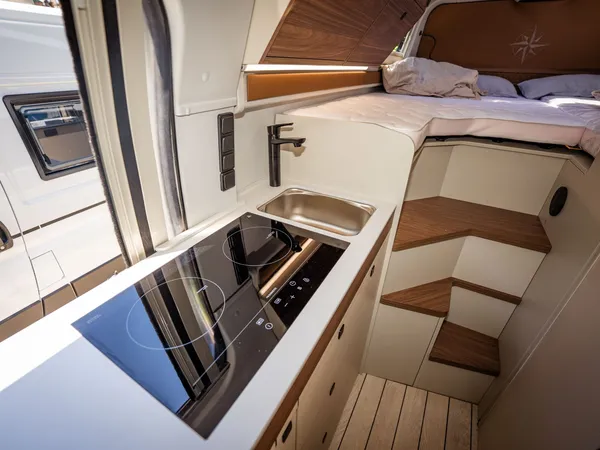 Columbus Liner – Moderne Küchenzeile mit Kochfeld, Spüle und Bett im Hintergrund