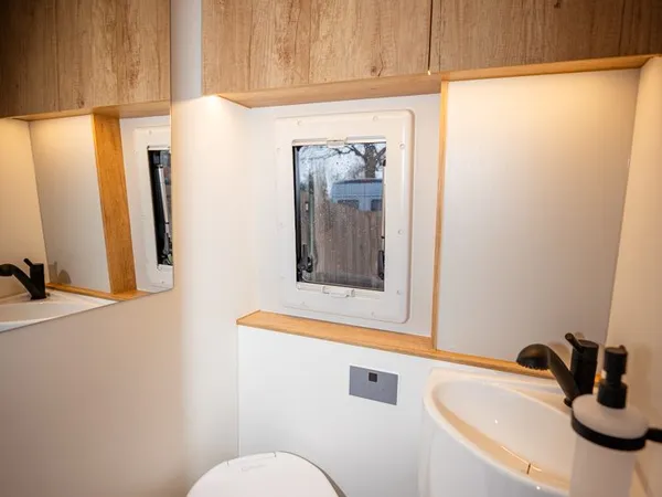 Avanti E – Blick ins Badezimmer mit Toilette, Waschbecken, Spiegel und Schränken.