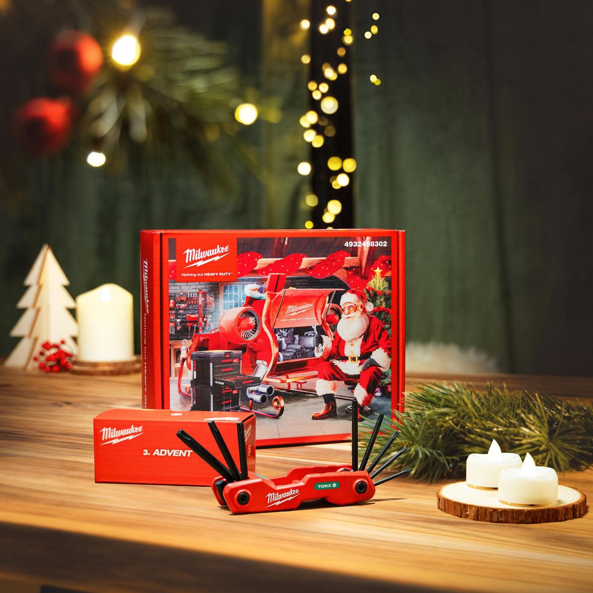 Milwaukee-Adventskalender mit Weihnachtsmann-Motiv auf Holztisch, davor die Box „3. Advent“ und ein roter Torx-Klappschlüsselsatz, dazu Kerzen, Tannenzweige und Lichterkette
