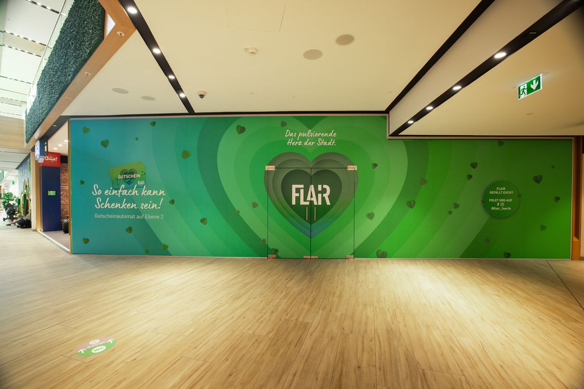 Großflächige grüne Wandgestaltung im FLAiR Fürth: Herz-Motiv mit FLAiR-Logo, Claim „Das pulsierende Herz der Stadt.“ und Gutschein-Hinweis