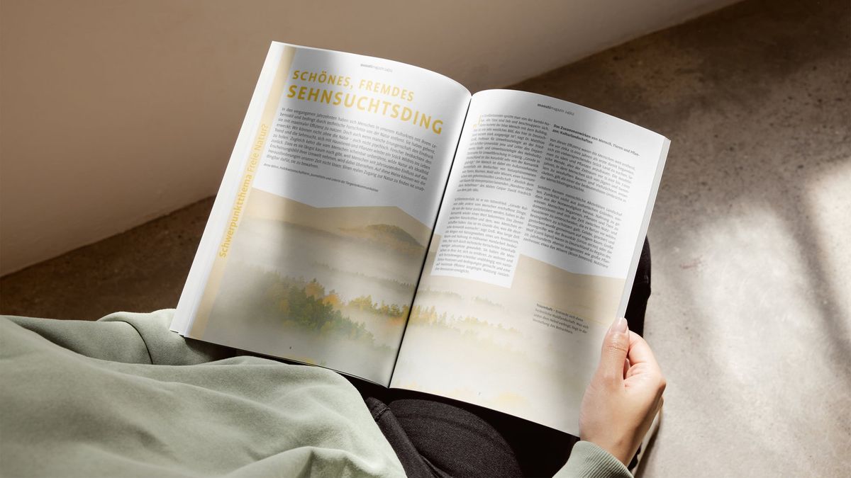 Person liest im aufgeschlagenen manatimagazin den Artikel „Schönes, fremdes Sehnsuchtsding“