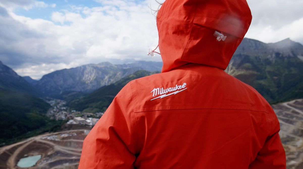 Person in roter Milwaukee-Regenjacke mit Kapuze von hinten, Blick über Tal, Ortschaft und Tagebau in die Berge
